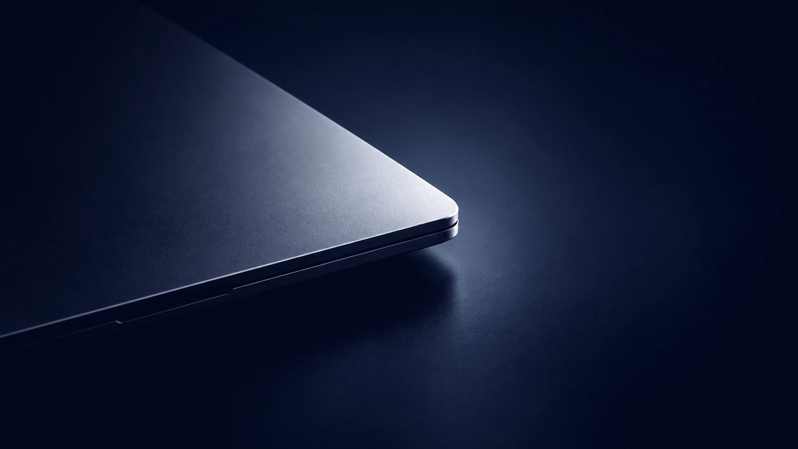 The edge of a dark laptop on a black surface, lit from the side